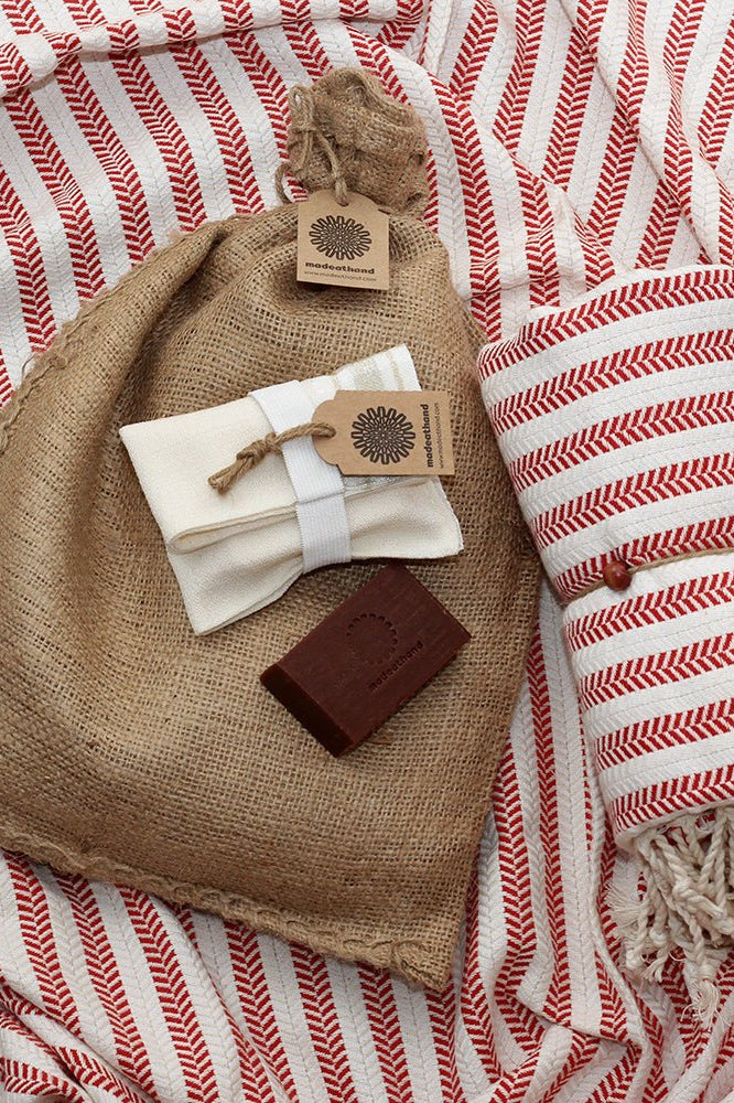 Hamamtuch aus 100 % Baumwolle in Rot mit feinem Fischgrätmuster und weißen Fransen, kombiniert mit einem Peeling Handschuh und roter Naturseife – stilvolles Wellness- und Reiseaccessoire von DENIO Home.