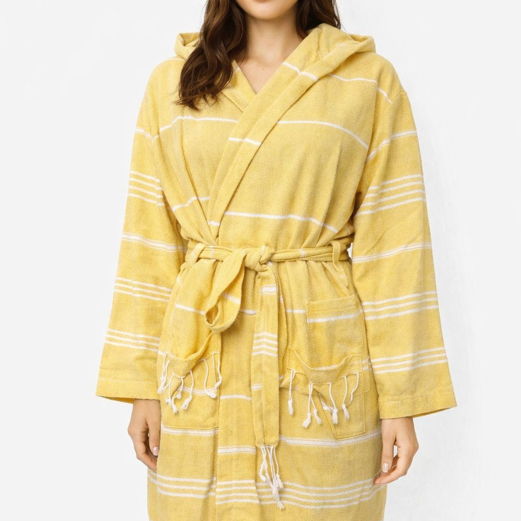 Frau trägt Bademantel in Farbe Gelb aus glatter Baumwolle mit weißen Streifen und Kapuze vor weißem Hintergrund.