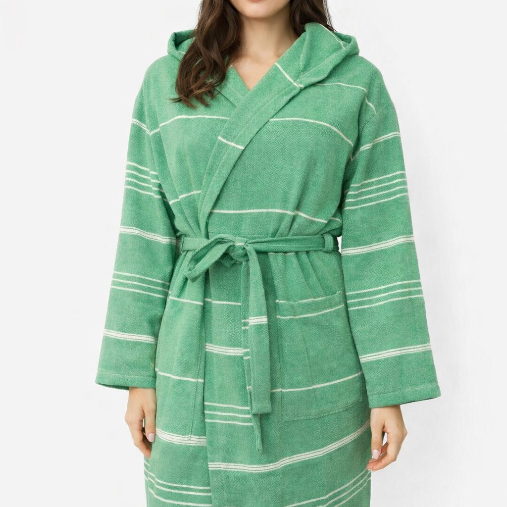 Frau trägt Bademantel in Farbe grün aus glatter Baumwolle mit weißen Streifen und Kapuze vor weißem Hintergrund.