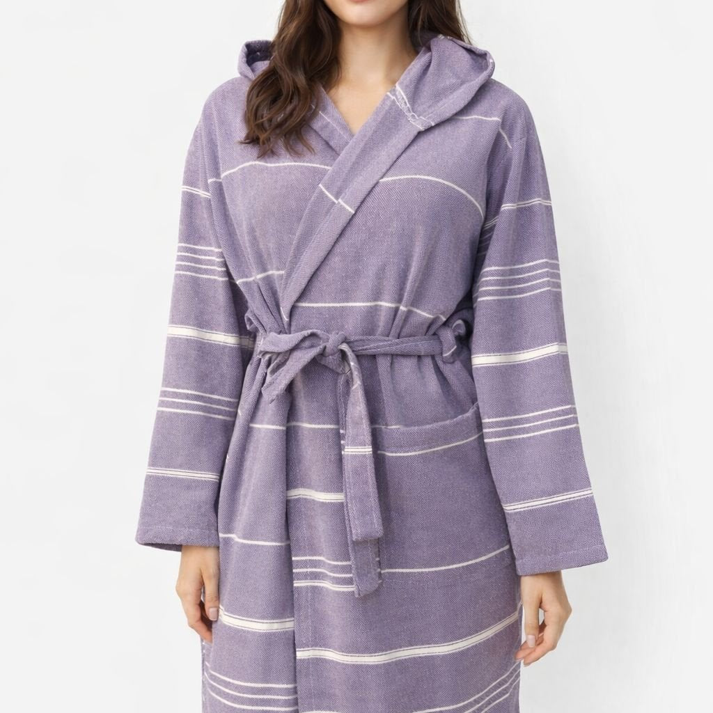 Frau trägt lila Bademantel aus glatter Baumwolle mit weißen Streifen und Kapuze vor weißem Hintergrund.