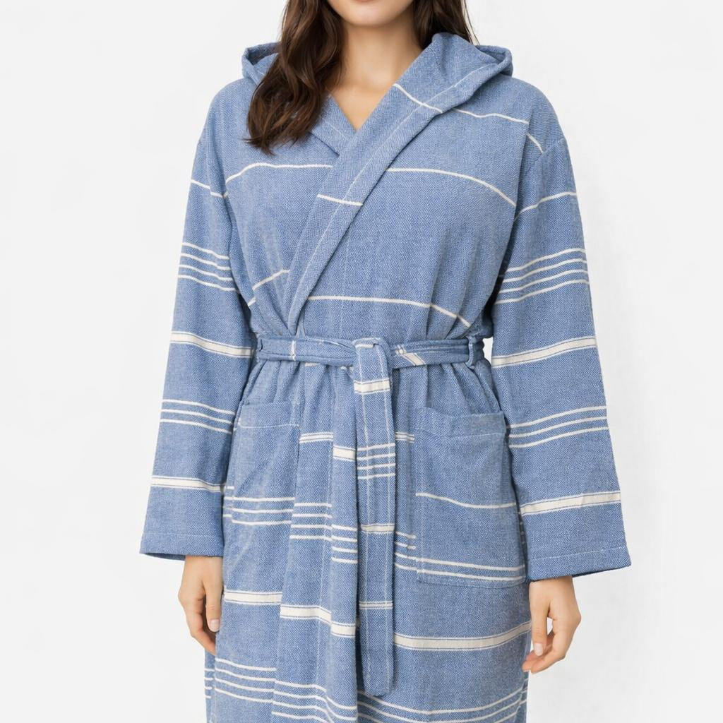 Frau trägt Bademantel in Farbe Saxblau aus glatter Baumwolle mit weißen Streifen und Kapuze vor weißem Hintergrund.