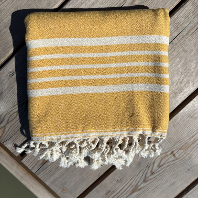 Hamamtuch ALMA – Dein vielseitiges Strandtuch für Sommer in Gelb zusammengelegt am Strand -DENIO