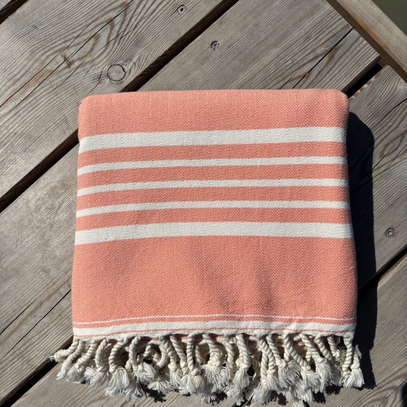 Hamamtuch ALMA – Dein vielseitiges Strandtuch für Sommer in Lachsrosa zusammengelegt am Strand -DENIO