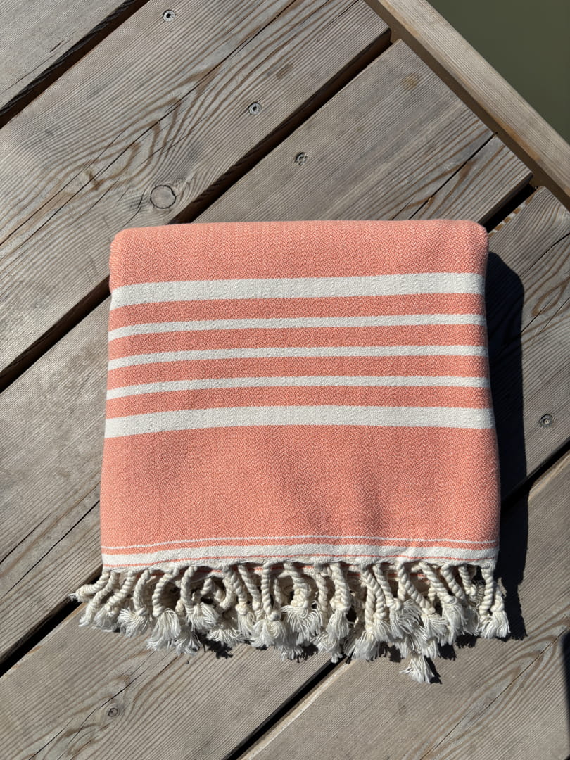 Hamamtuch ALMA – Dein vielseitiges Strandtuch für Sommer in Lachsrosa zusammengelegt am Strand -DENIO