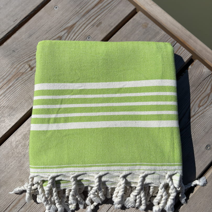 Hamamtuch ALMA – Dein vielseitiges Strandtuch für Sommer in Limette zusammengelegt am Strand -DENIO