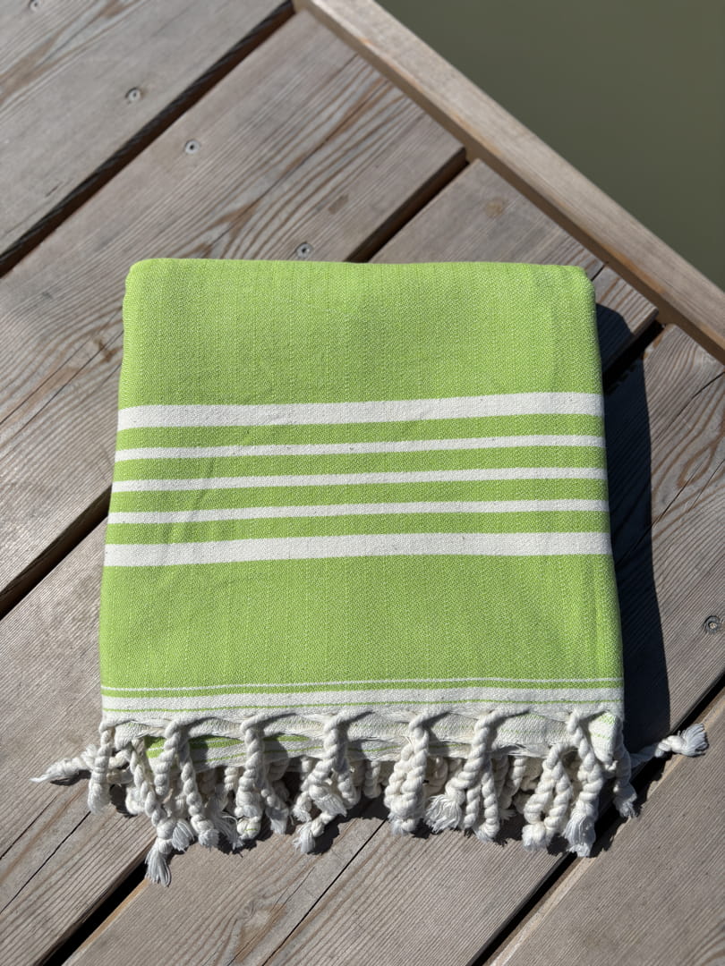 Hamamtuch ALMA – Dein vielseitiges Strandtuch für Sommer in Limette zusammengelegt am Strand -DENIO