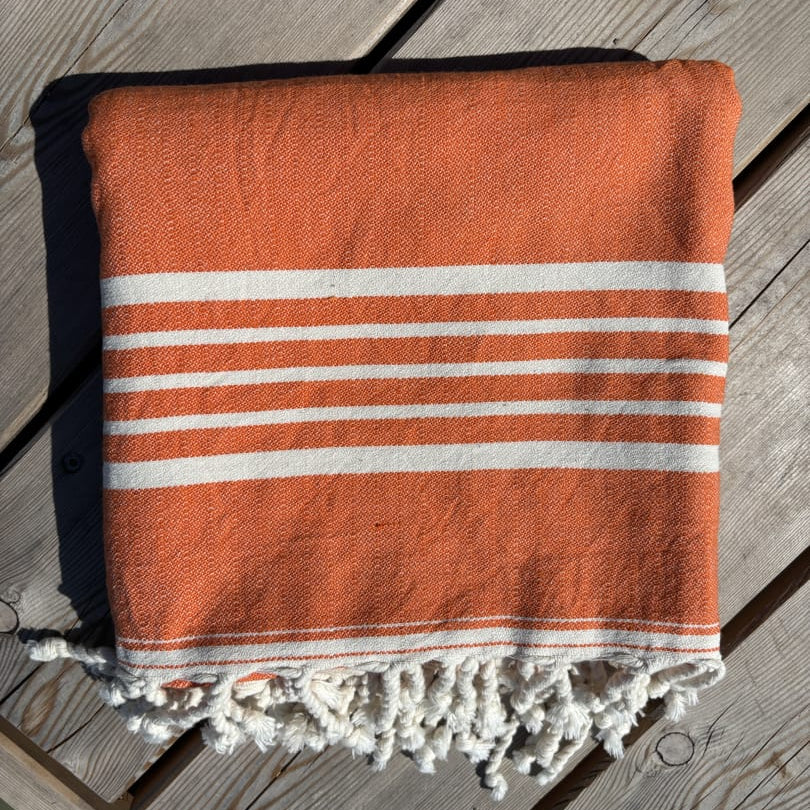 Hamamtuch ALMA – Dein vielseitiges Strandtuch für Sommer in Orange zusammengelegt am Strand -DENIO