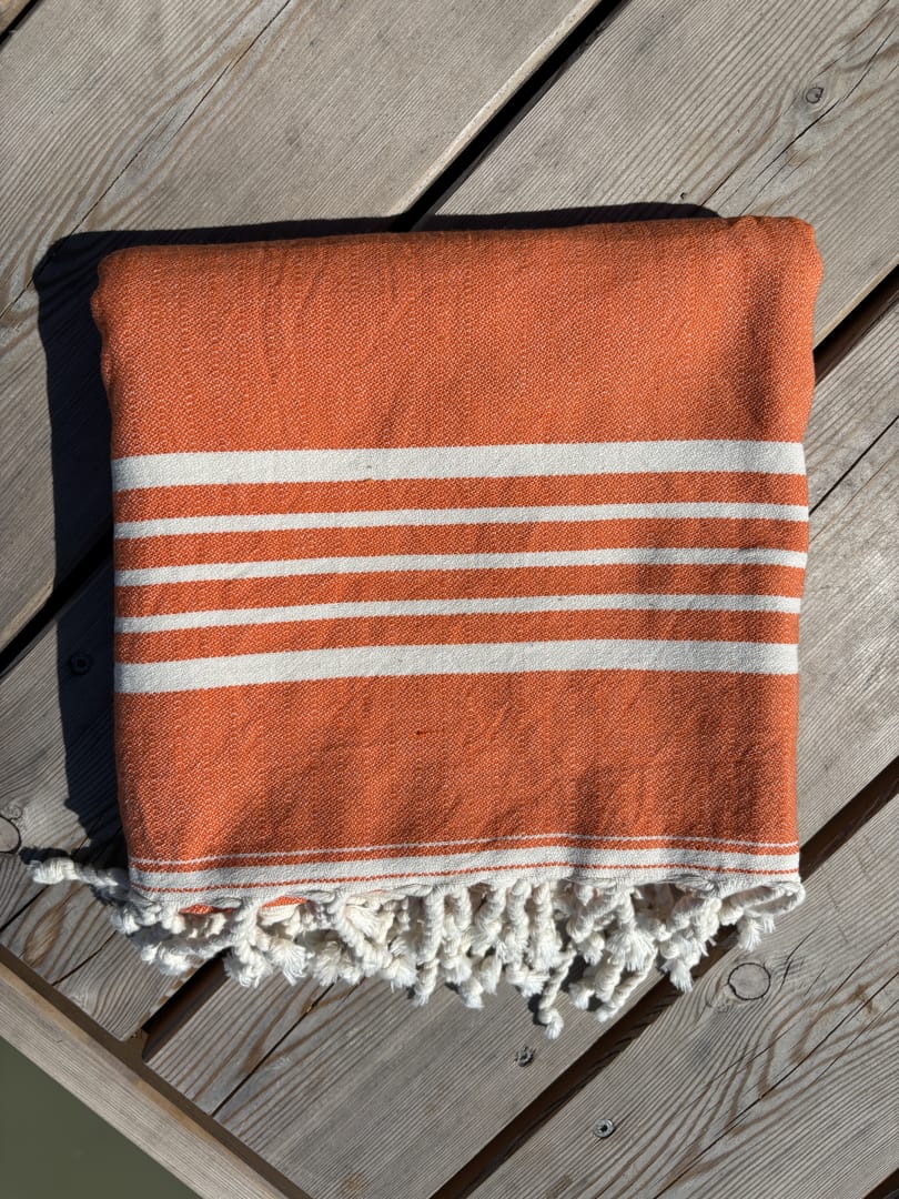 Hamamtuch ALMA – Dein vielseitiges Strandtuch für Sommer in Orange zusammengelegt am Strand -DENIO