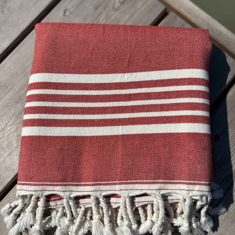 Hamamtuch ALMA – Dein vielseitiges Strandtuch für Sommer in Rot zusammengelegt am Strand -DENIO