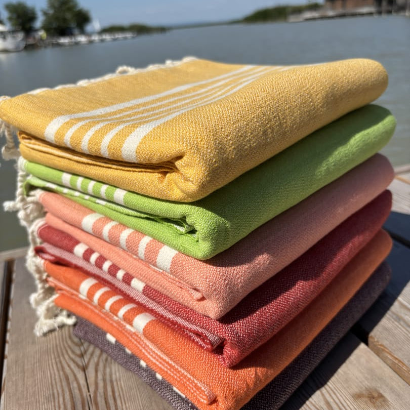 Hamamtuch ALMA – Strandtücher für Sommer in Farben Gelb, Limette, Lachsrosa, Rot, Orange und Dunkelbraun zusammengelegt am Strand -DENIO