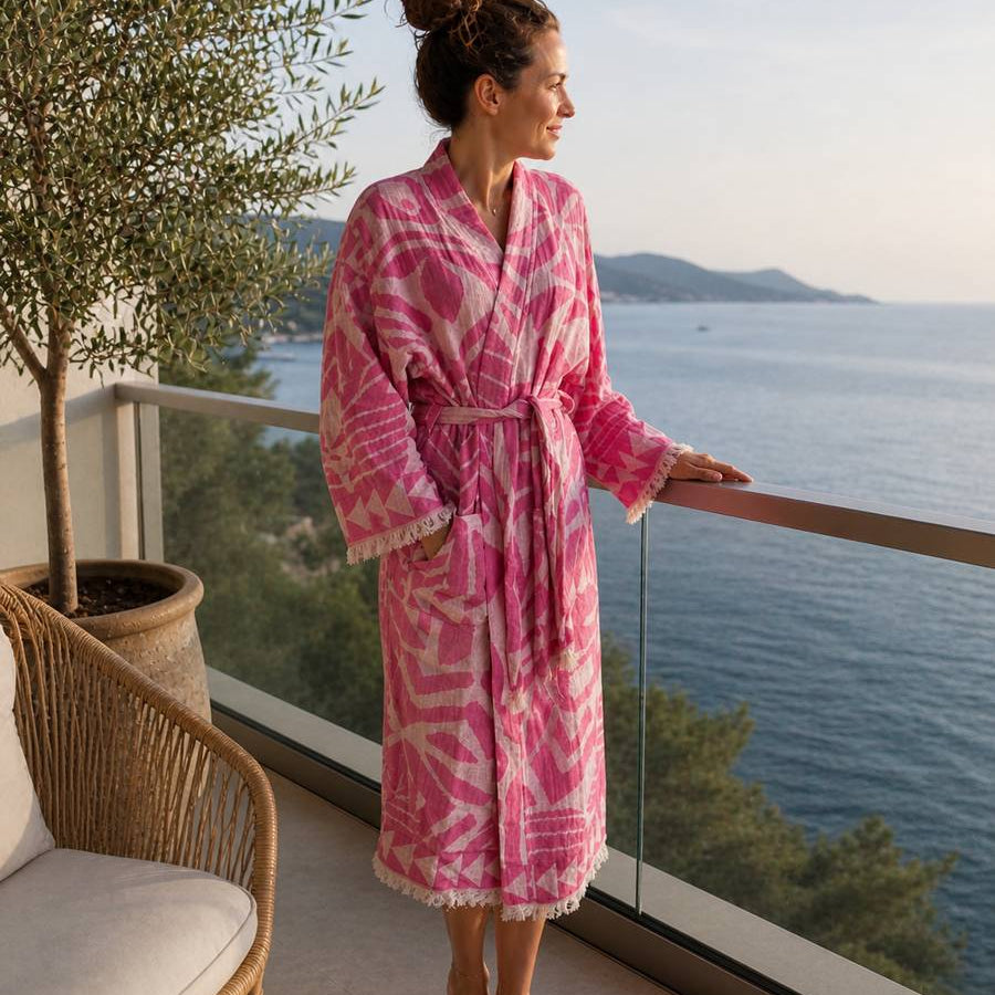 Eine Frau steht am Balkon mit Blick ans Meer und trägt einen Leichten Bademantel in Pink