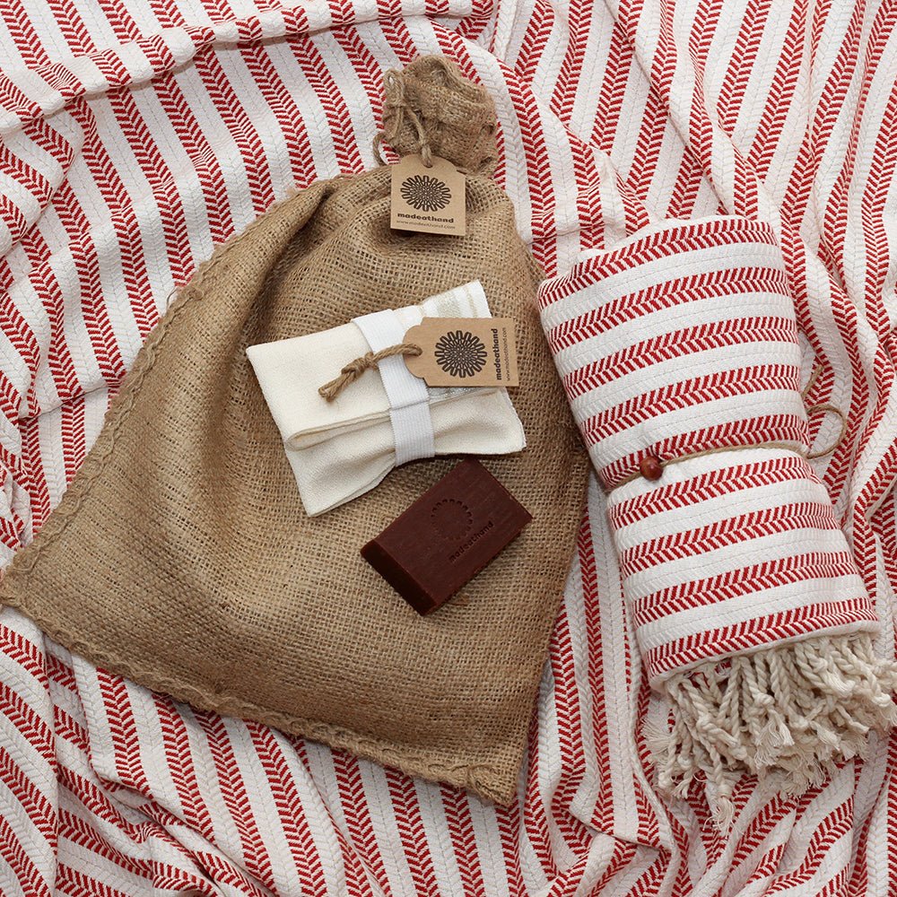 Hamamtuch aus 100 % Baumwolle in Rot mit feinem Fischgrätmuster und weißen Fransen, kombiniert mit einem Peeling Handschuh und roter Naturseife – stilvolles Wellness- und Reiseaccessoire von DENIO Home.