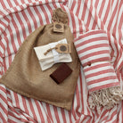 Hamamtuch aus 100 % Baumwolle in Rot mit feinem Fischgrätmuster und weißen Fransen, kombiniert mit einem Peeling Handschuh und roter Naturseife – stilvolles Wellness- und Reiseaccessoire von DENIO Home.