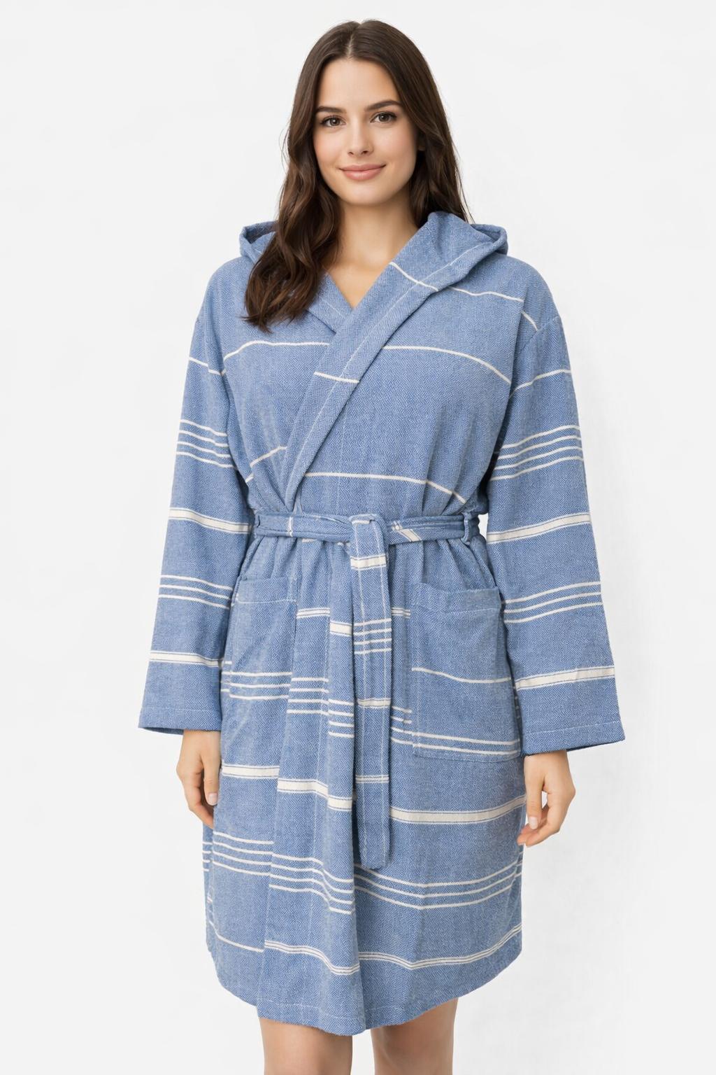 Frau trägt Bademantel in Farbe Saxblau aus glatter Baumwolle mit weißen Streifen und Kapuze vor weißem Hintergrund.