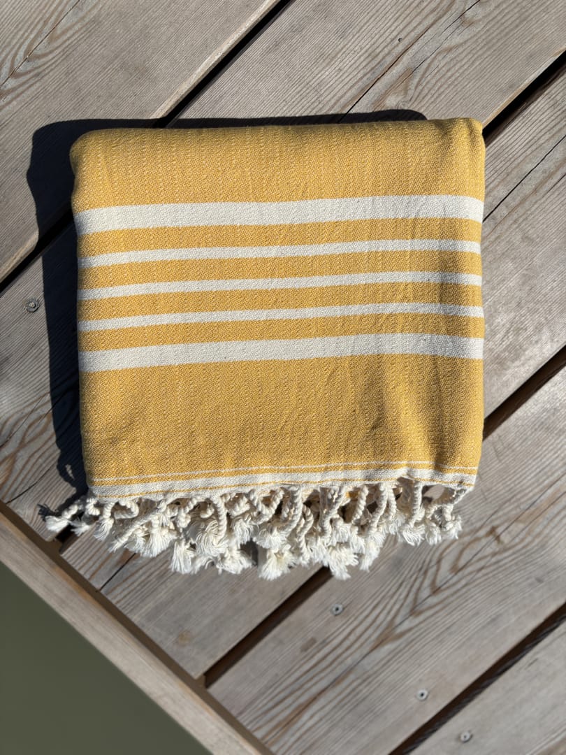 Hamamtuch ALMA – Dein vielseitiges Strandtuch für Sommer in Gelb zusammengelegt am Strand -DENIO