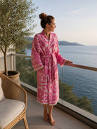 Eine Frau steht am Balkon mit Blick ans Meer und trägt einen Leichten Bademantel in Pink